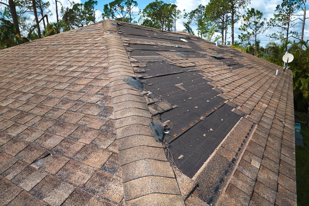 Damaged house roof with missing shingles after hurricane Ian in Florida. Consequences of natural disaster